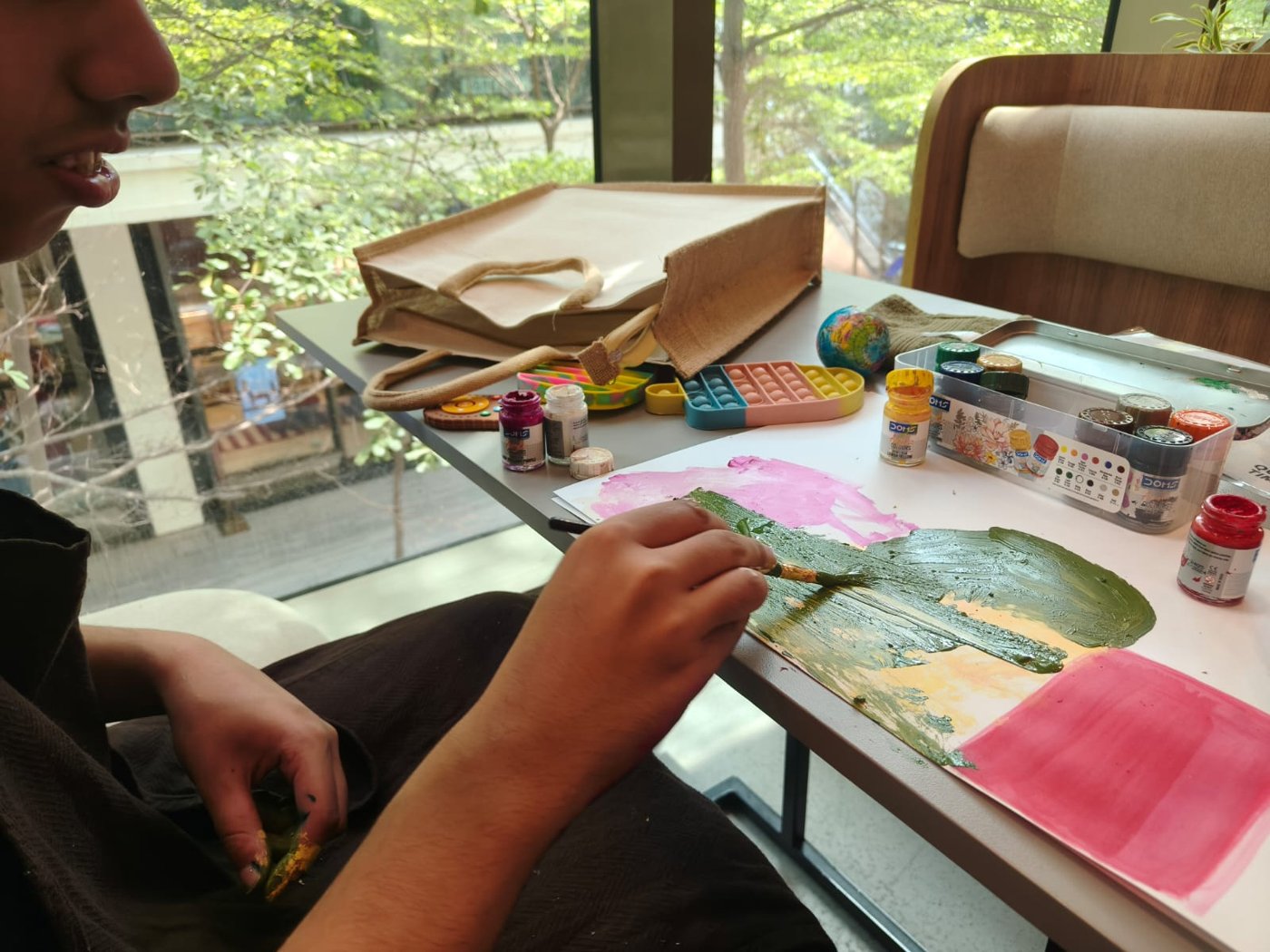 Close-up of Vivaan's hands painting green leaves at a table covered with paints