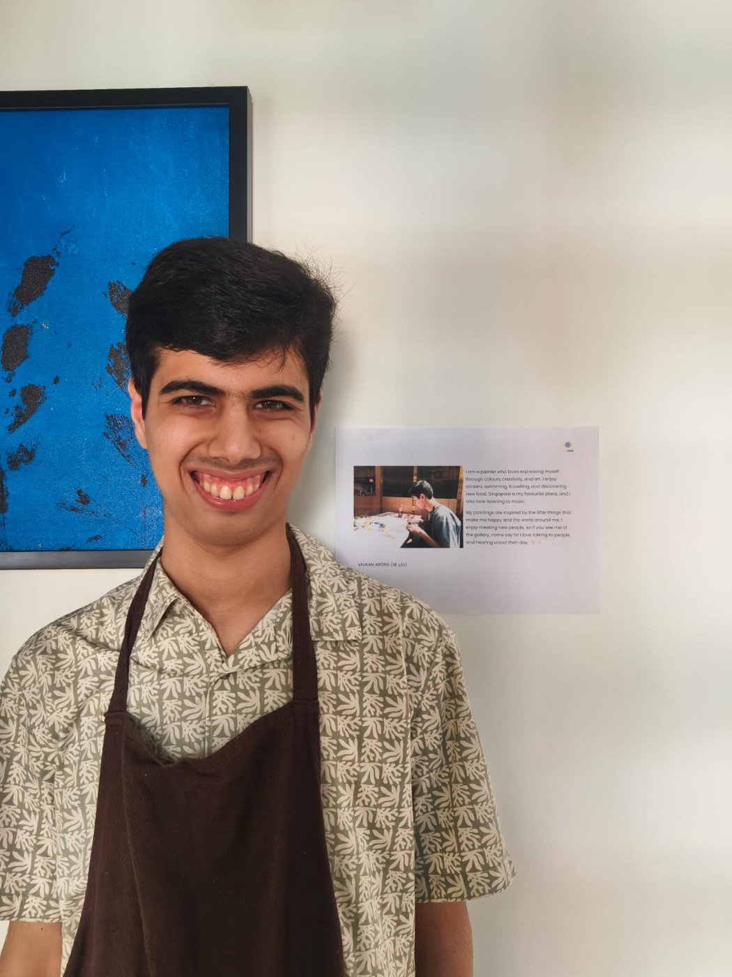 Vivaan smiling in a brown painting apron, standing beside Blue Leaves